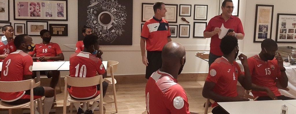 Members of the national training squad listen attentively as restaurant owner Adam Aboud, right, and coach Terry Fenwick address them yesterday at Adam's Gourmet Restaurant and Bakery in Maraval.